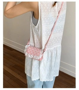 Close-up of pink polka dot crossbody bag with white lace trim worn by a child