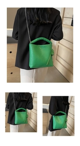 Detail of green woven bucket bag showing the texture, heart charm, and silver chain strap