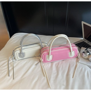 Detail of cream and pink faux leather baguette bags with long tassel zippers on a desk