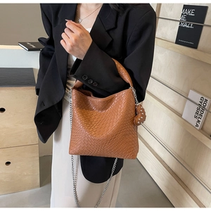Detailed view of caramel brown woven bucket bag featuring metal chain and heart charm