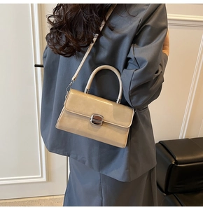 Detailed side view of beige leather crossbody bag with silver lock worn by model