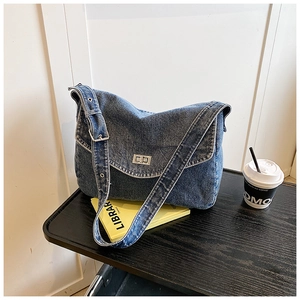 Dettaglio borsa tote in denim blu con chiusura girevole in metallo argentato su un tavolo