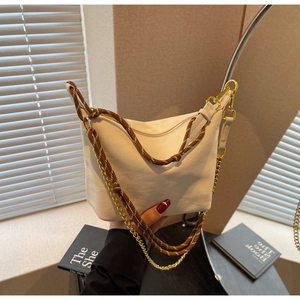 Detail of cream canvas dumpling bag featuring woven brown rope and gold chain strap