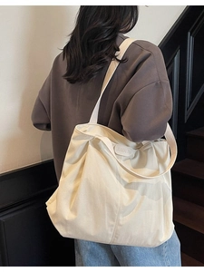 Minimalist cream canvas tote bag with wide strap worn by model in urban setting