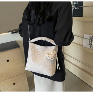 Detail of woven texture bucket bag in creamy white with a heart charm and chain strap