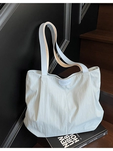 Large light blue nylon tote bag with dual straps on a minimalist urban step setting