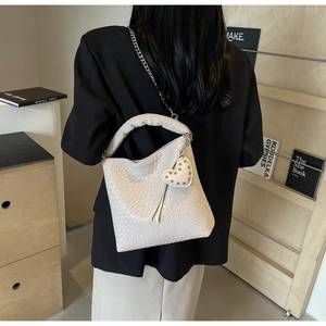 Detail view of beige woven bucket bag with silver chain strap and heart charm on a model