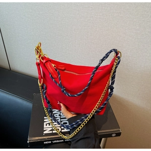 Detail of red nylon crescent bag with gold chain and blue-white braided strap