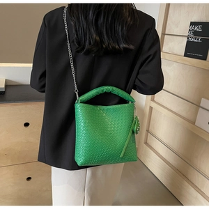 Detail of green crocodile texture bucket bag with twisted handle on a model in a black blazer