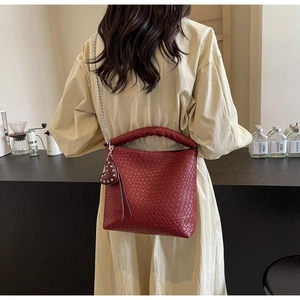 Detail of burgundy woven bucket bag with silver chain strap and heart charm on a model