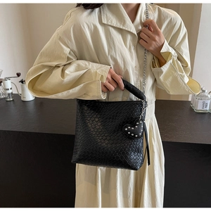 Detail of black woven bucket bag with silver chain strap and heart charm on a model