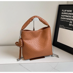 Detail of warm brown woven bucket bag featuring heart rivet charm and silver chain strap
