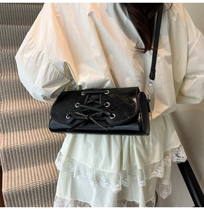 Detail of black patent leather shoulder bag with lace-up design and silver metal rings