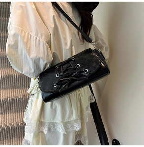 Detail of black glossy shoulder bag featuring cross-lace design and silver eyelets