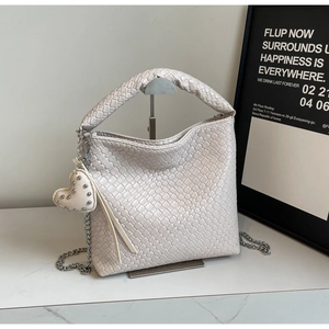 Detailed close-up of woven beige bucket bag with heart rivet charm and metal chain