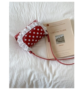 Detail of red polka dot crossbody bag with delicate white lace trim on gloss leather