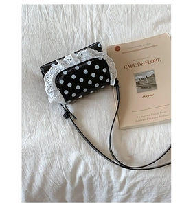 Close-up of retro black polka dot crossbody bag with white lace trim on white fabric