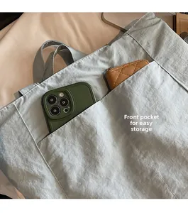 Close-up of light grey-blue tote bag showing two front pockets for smartphone storage