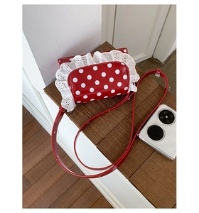 Detailed view of red polka dot crossbody bag with white lace trim and leather strap