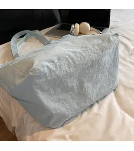 Detail view of a light blue nylon tote bag with textured fabric on a bed with a laptop
