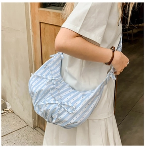 Detailed view of striped crossbody bag with bow accents and soft pleats on white dress