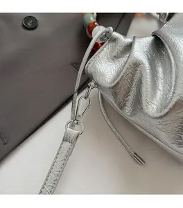 Detail of silver pleated bucket bag with acrylic beads handle and metallic hardware