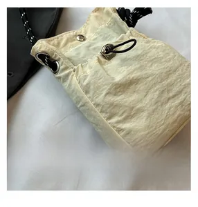 Detailed macro view of cream nylon bucket bag with metal eyelets and woven drawstring textures