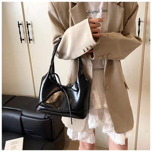 Detail of glossy black PU tote bag with bow accent worn over the shoulder by model
