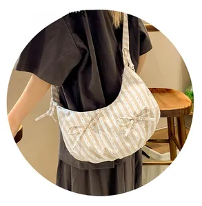 Close-up of beige striped canvas dumpling bag featuring cute decorative ribbon bows