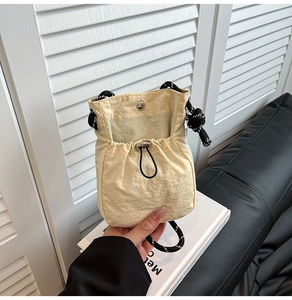 Close-up of beige drawstring nylon bucket bag with a black and white woven rope strap