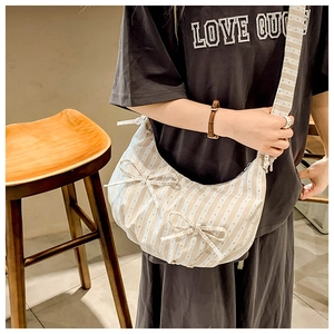 Detail of striped dumpling bag with bow accents and wide canvas shoulder strap for women