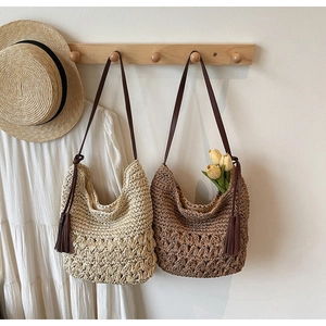 Détail de sacs cabas en paille tissée avec anses en cuir et pompons style vacances