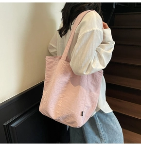 Detail view of light pink nylon tote bag with minimalist side tag and wrinkled texture