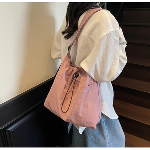 Pink drawstring bucket bag worn over the shoulder showing side pocket and nylon texture