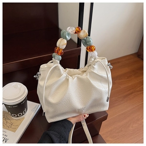 Detailed view of cream pleated bucket bag with decorative translucent beaded handle