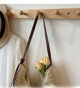 Détail d'un sac cabas en paille tissée avec fine bandoulière en cuir marron et fleurs