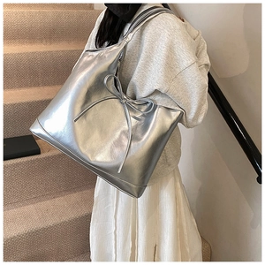 Close-up of a large silver PU leather tote bag with bow detail worn by a model