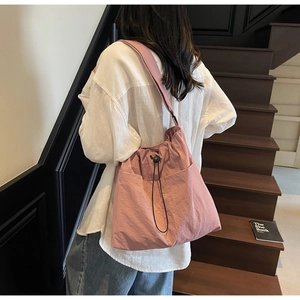 Detail view of pink drawstring bucket bag with side pocket on a model by stairs