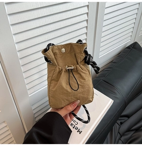 Detail showing the khaki drawstring bucket bag with textured fabric and woven rope strap
