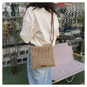 Detail of hand-woven beige straw crossbody bag with brown leather tag and slim strap