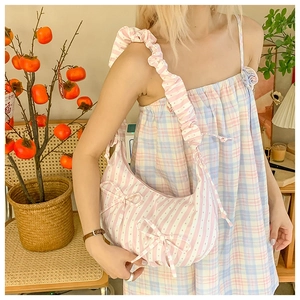 Detail of pink striped hobo bag with bow accents and ruffled strap worn by model