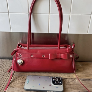 Detail of red glossy shoulder bag with ribbon bow and silver heart pendant charm
