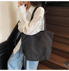 Minimalist black tote bag shown on shoulder with spacious side pockets and light fabric