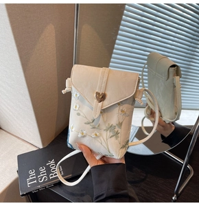 Vue détaillée de la broderie marguerite et du fermoir cœur sur un sac de téléphone beige