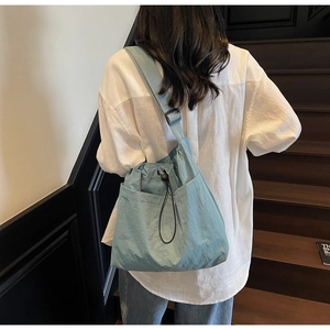 Detail view of light blue nylon crossbody bag shown from a side angle on a model