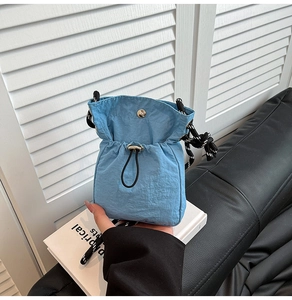 Detail of sky blue nylon drawstring bag with black and white striped rope and metal button