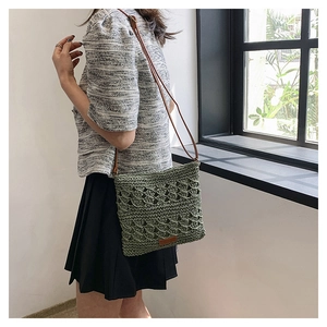 Detail of woven straw crossbody bag in green with leather strap and logo patch