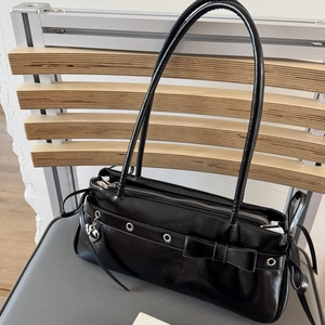 Detail view of black glossy shoulder bag with bow decor and silver heart pendant
