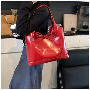Detail of red glossy PU leather tote bag with bow accent and large shoulder strap