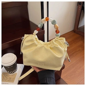 Detail of light yellow ruched bucket bag with colorful beaded handle and leather texture